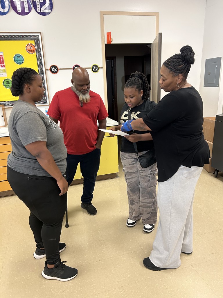 A student stands with her family and teacher, reviewing a paper together during a student-led conference in the classroom.
