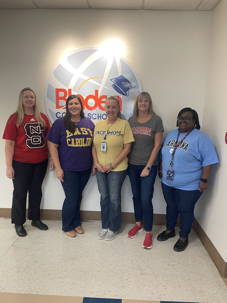 Five women stand in front of the Bladen County Schools logo, each wearing a college-themed shirt representing NC State, East Carolina, UNCP, Alabama, and Arizona.