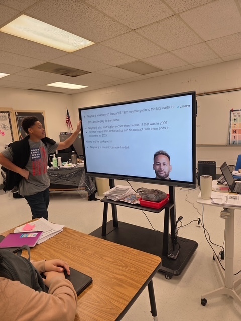 A student presents a slide about Brazilian soccer player Neymar Jr., which includes his photo and biographical information.