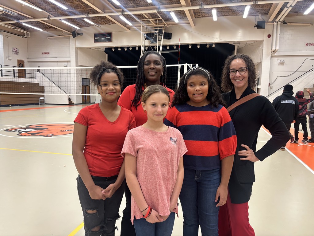 A group of five people stand together in the Elizabethtown Middle School gym. Two adults and three students smile for the camera in front of the volleyball net and Cougar logo on the court. The students are wearing red, showing school spirit.