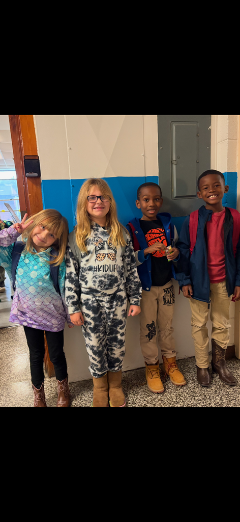 Four students stand in a hallway smiling and making peace signs while showing off their boots and fall outfits.