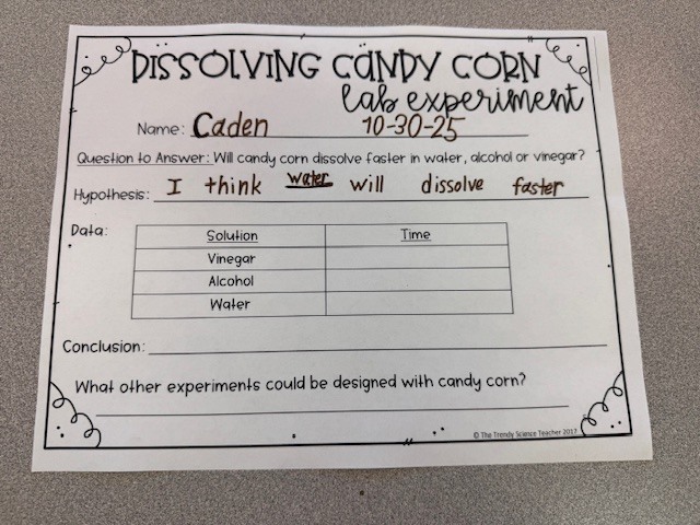 A printed instruction sheet titled “Dissolving Candy Corn Student Instructions.” It lists the materials needed—alcohol, water, vinegar, candy corn, and cups—and outlines steps for labeling cups, adding solutions, timing the dissolving process, and completing a lab sheet.