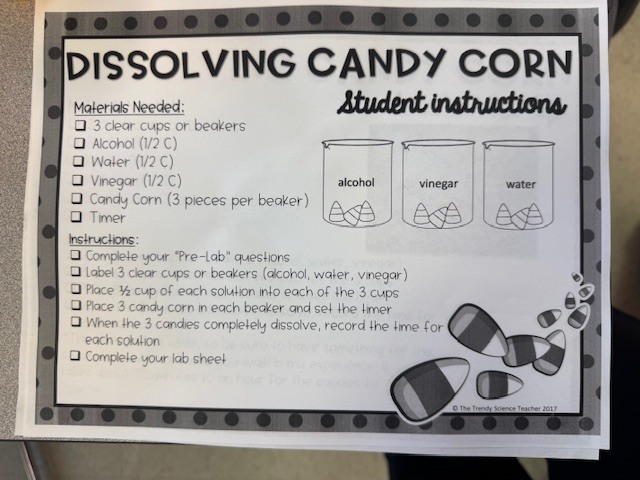 A close-up of a student’s completed “Dissolving Candy Corn Lab Experiment” worksheet. The student, named Caden, hypothesized that candy corn would dissolve faster in water, and there are spaces for recording data on vinegar, alcohol, and water solutions.