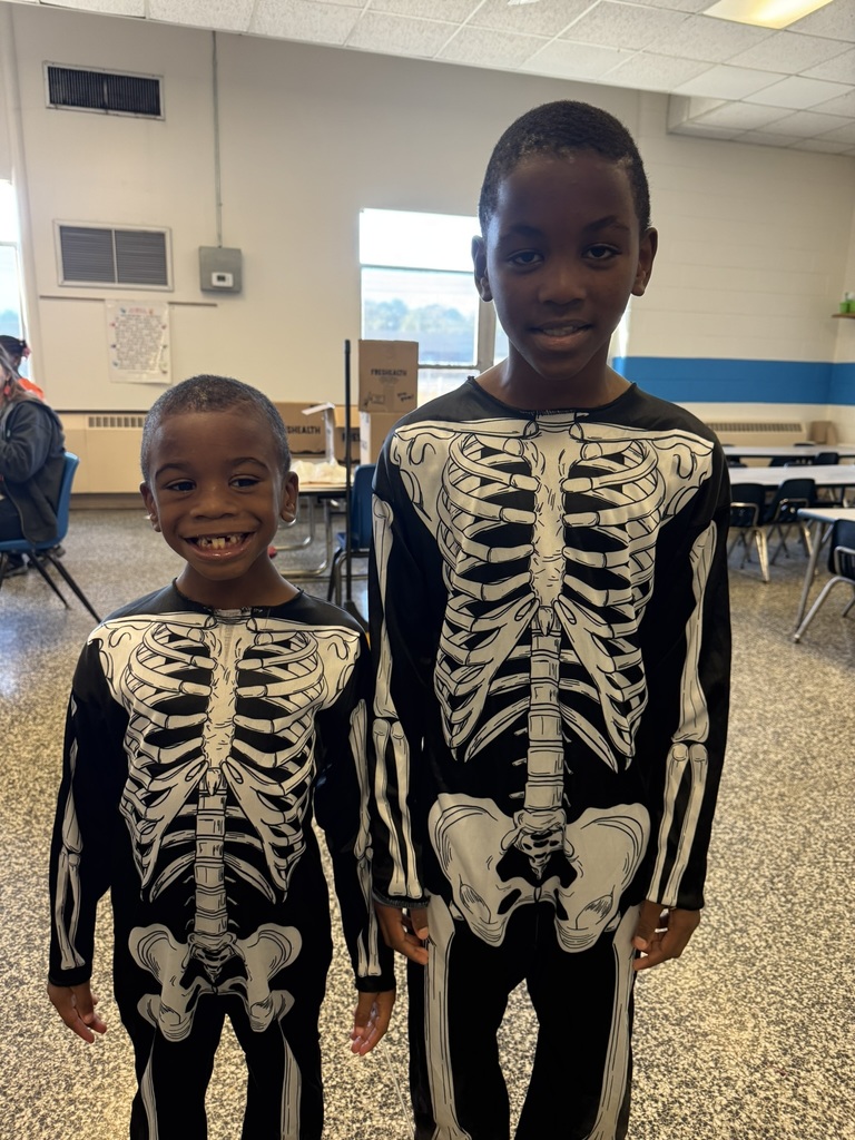 Two students wearing matching black skeleton costumes, smiling in a classroom.