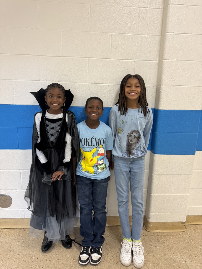 Three students standing together; one dressed as a vampire, another in a Pokémon shirt, and the third in a light blue outfit with a drawing of a girl.Three students standing together; one dressed as a vampire, another in a Pokémon shirt, and the third in a light blue outfit with a drawing of a girl.