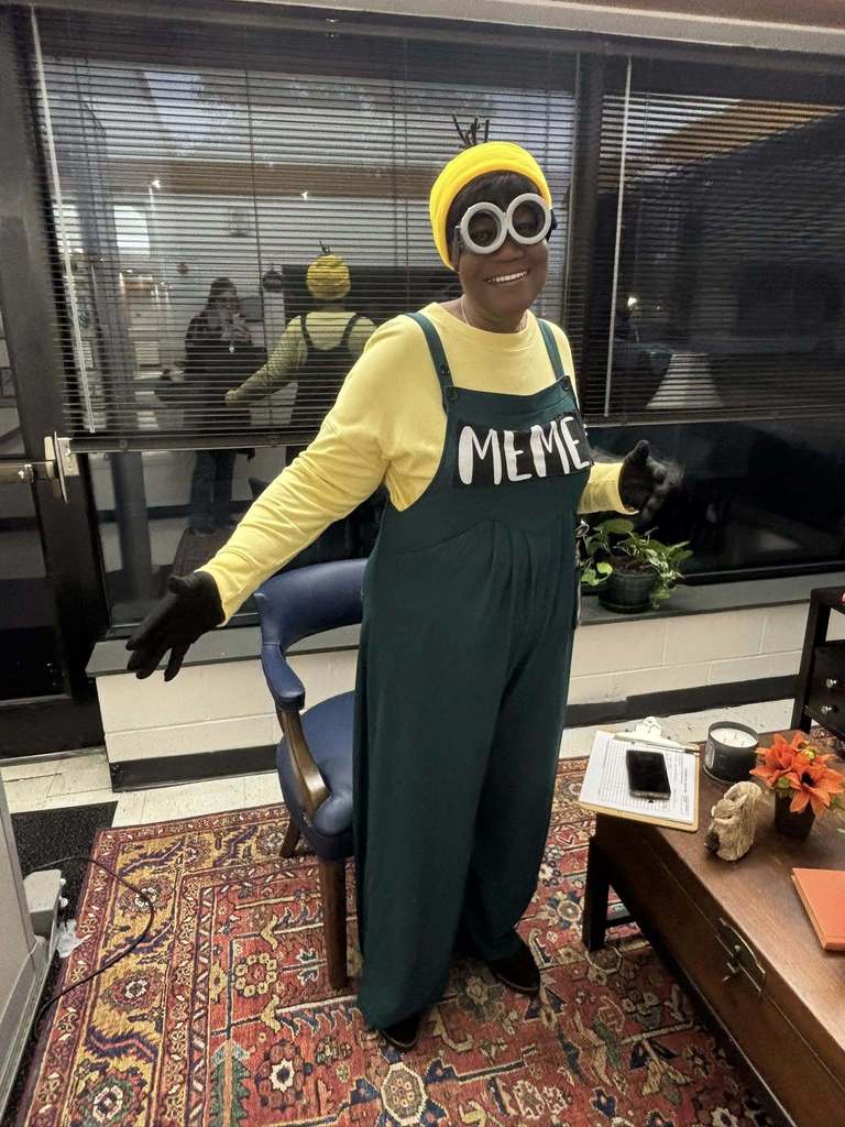 A staff member dressed as a Minion with yellow hat, goggles, and green overalls smiles.