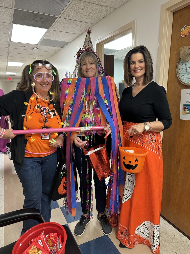 Three staff members in festive Halloween attire stand together with candy buckets and decorations.