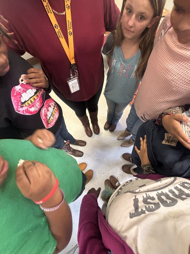 A close-up, top-down view of a circle of students and a teacher showing their boots and shoes as they stand together for a Red Ribbon Week group photo.