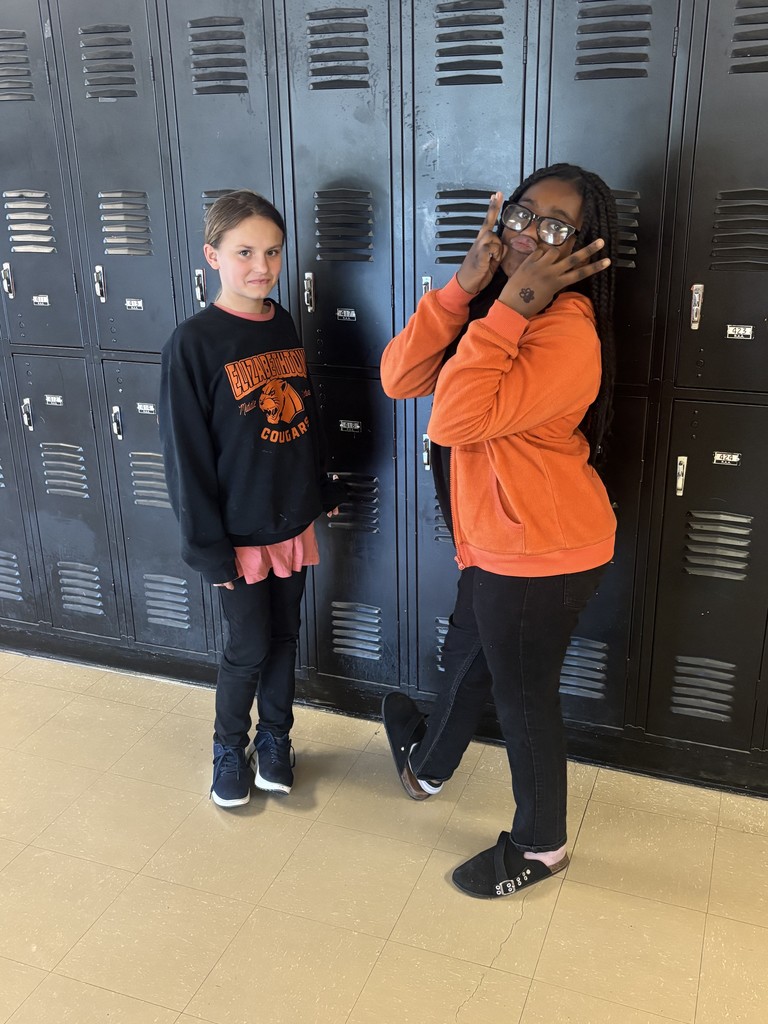 Two Elizabethtown Middle School students stand in front of black lockers. Both wear school colors—one in a black Cougar sweatshirt and the other in an orange jacket—smiling and posing playfully for Red Ribbon Week