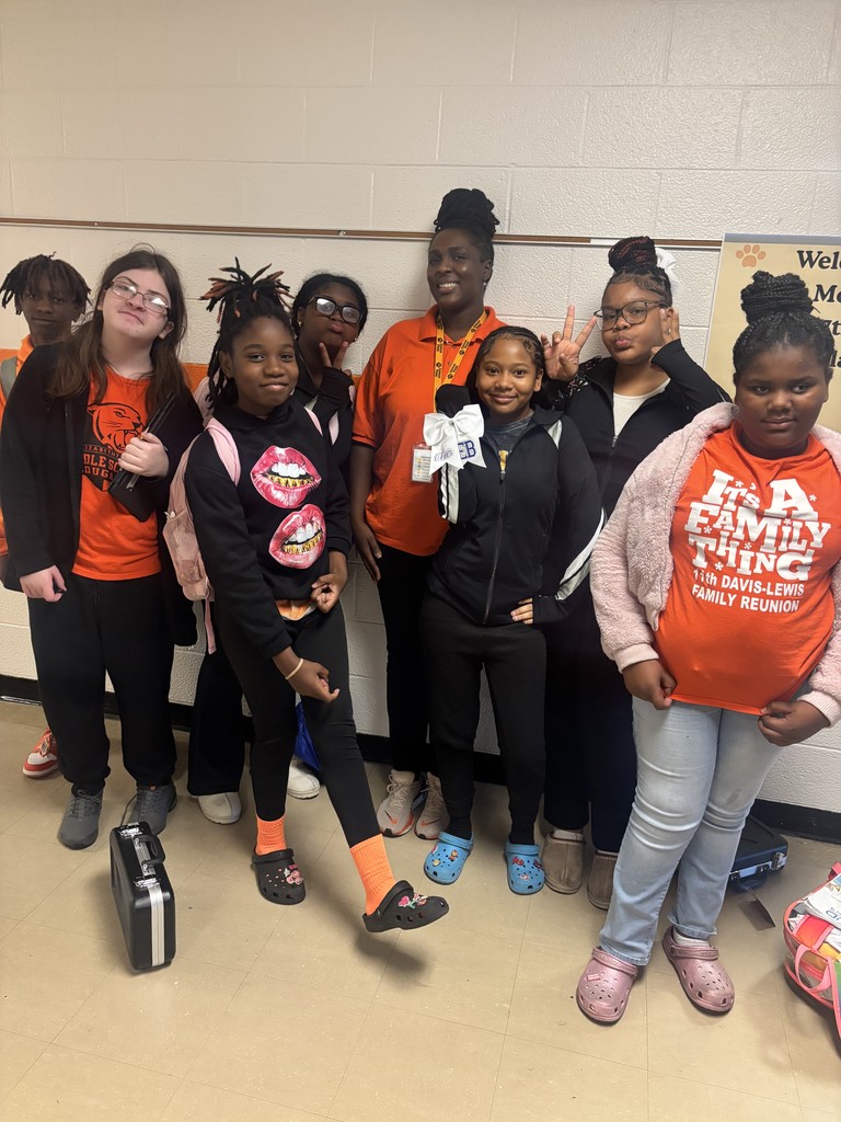 A group of students and a staff member smile in the hallway, wearing orange and black to show Cougar pride during Red Ribbon Week. The group poses together near a wall decorated in school colors.
