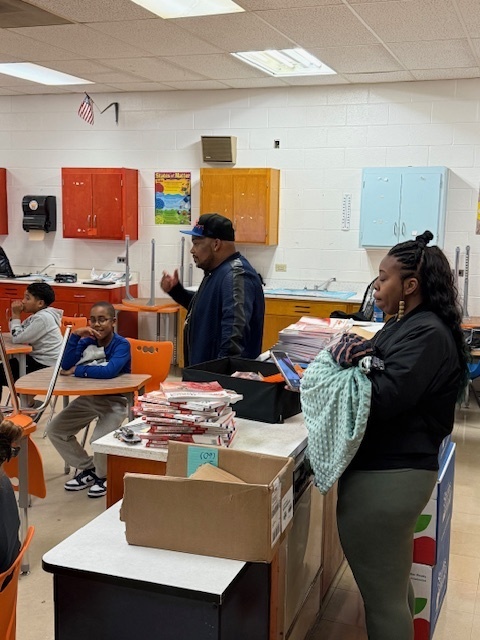 A teacher and parent help organize certificates and materials for students during the awards event inside a classroom.
