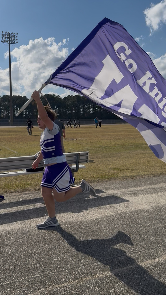 A student in a purple cheer uniform runs, holding a large flag that reads "Go Knights