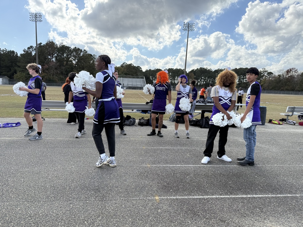 Cheerleaders in purple and white uniforms stand on a track next to a football field