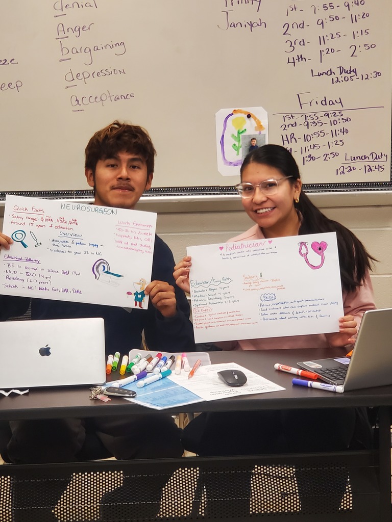 Two smiling students hold up handmade posters detailing the careers of a Neurosurgeon and a Pediatrician.