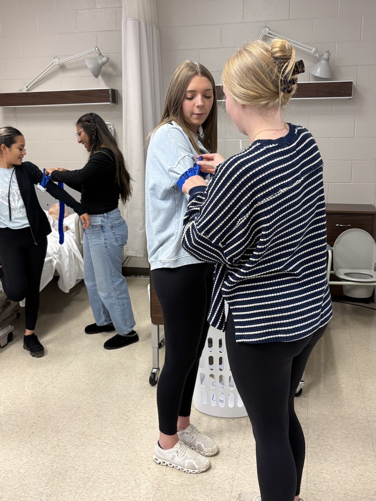 Students practice applying medical wraps to each other's arms in a classroom setting designed like a patient care lab