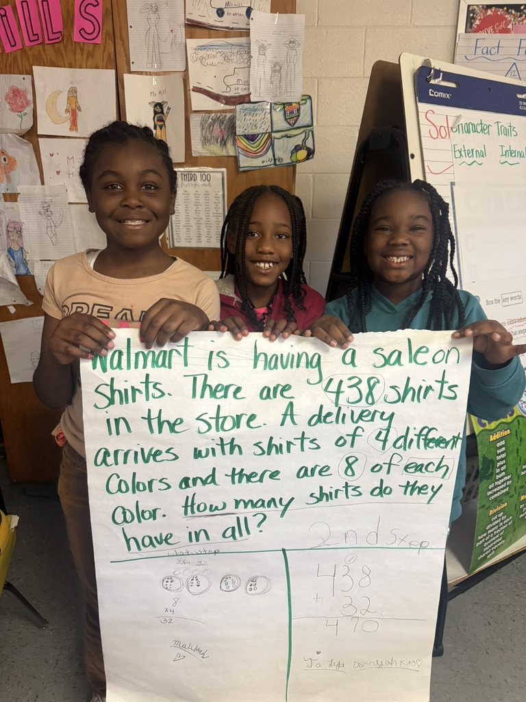 Small groups of smiling students hold up their completed chart paper showing their two-step word problems and written solutions. Each group stands proudly in their classroom, displaying their math work and teamwork.