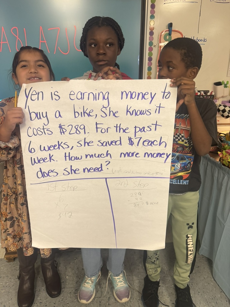 Small groups of smiling students hold up their completed chart paper showing their two-step word problems and written solutions. Each group stands proudly in their classroom, displaying their math work and teamwork.