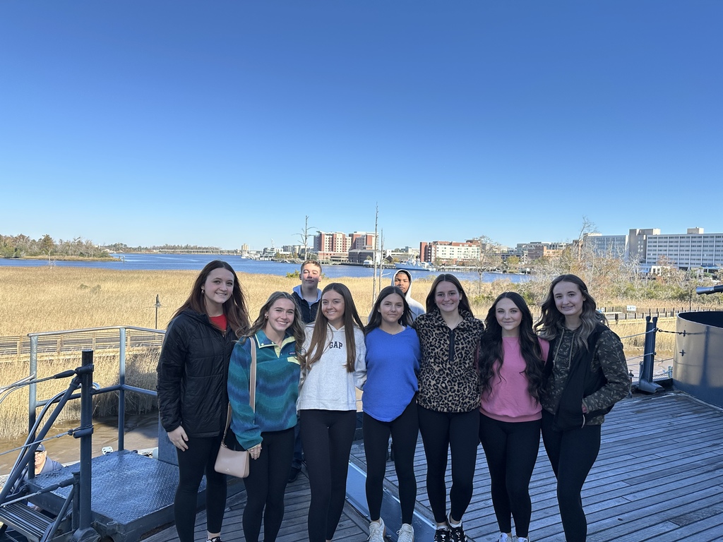 Group of high school students on the deck of a ship with a city skyline and marsh behind them.