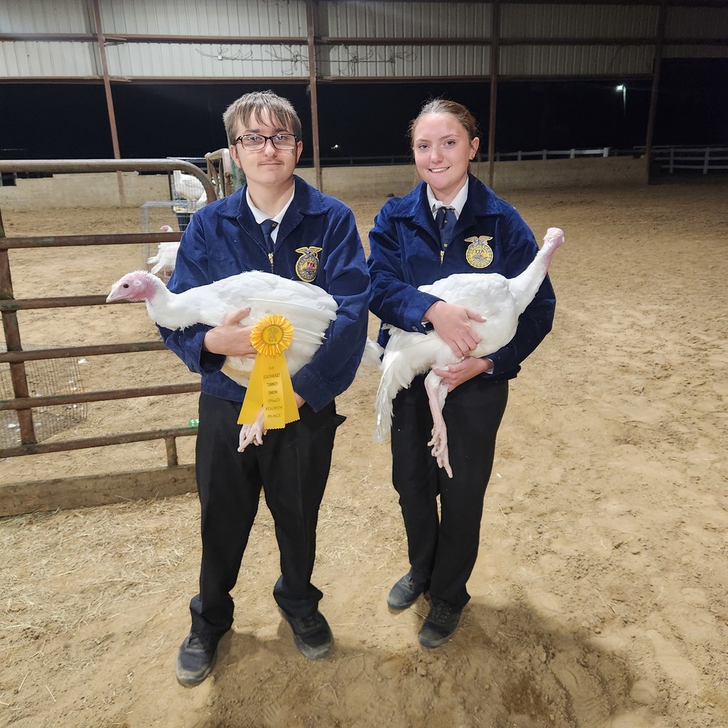 Two FFA students hold their white show turkeys; one turkey has a yellow award ribbon