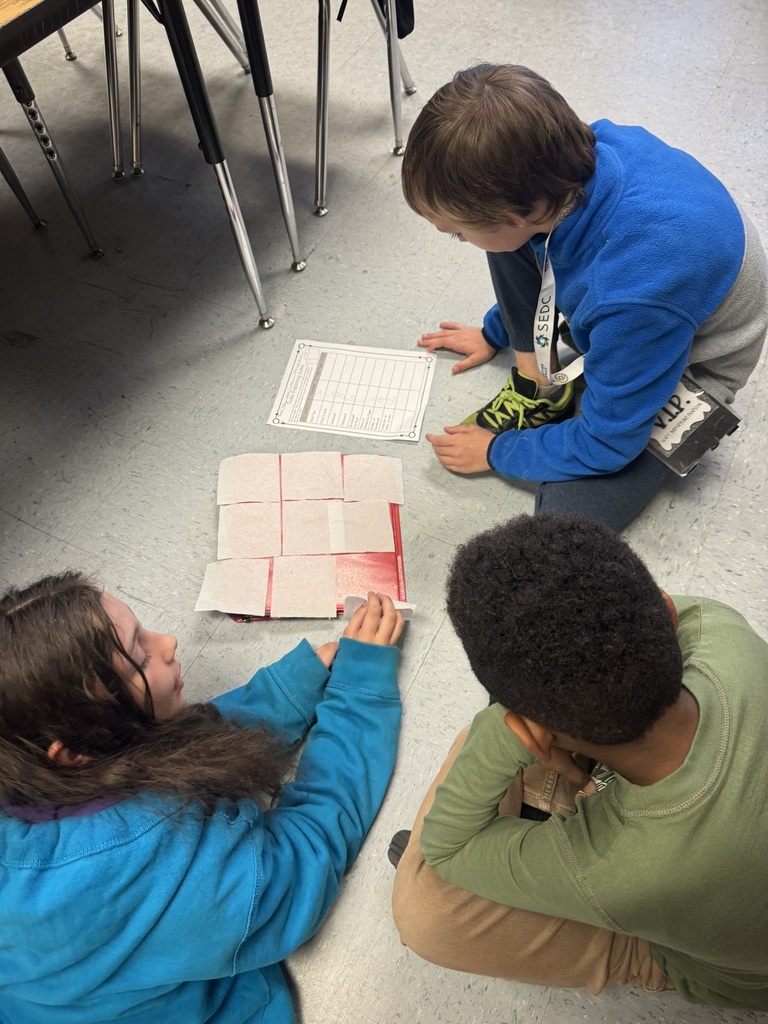 Three students sit on the floor measuring a book with toilet paper squares, using a recording sheet. In another photo, children stand around a desk layering squares to cover the surface. Additional photos show students carefully lining up squares and a full table covered in grid-patterned toilet paper pieces. One student kneels by a bookshelf measuring its area with the squares.