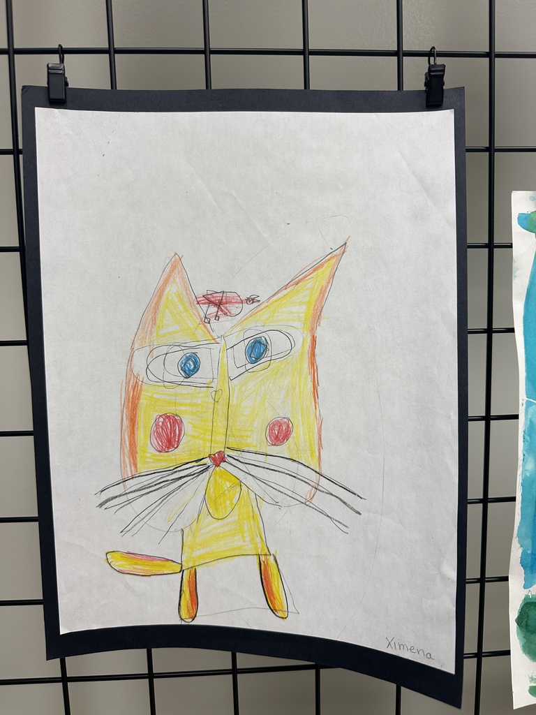 A child’s drawing of a yellow and orange cat with large blue eyes and a small red bug perched on its head.
