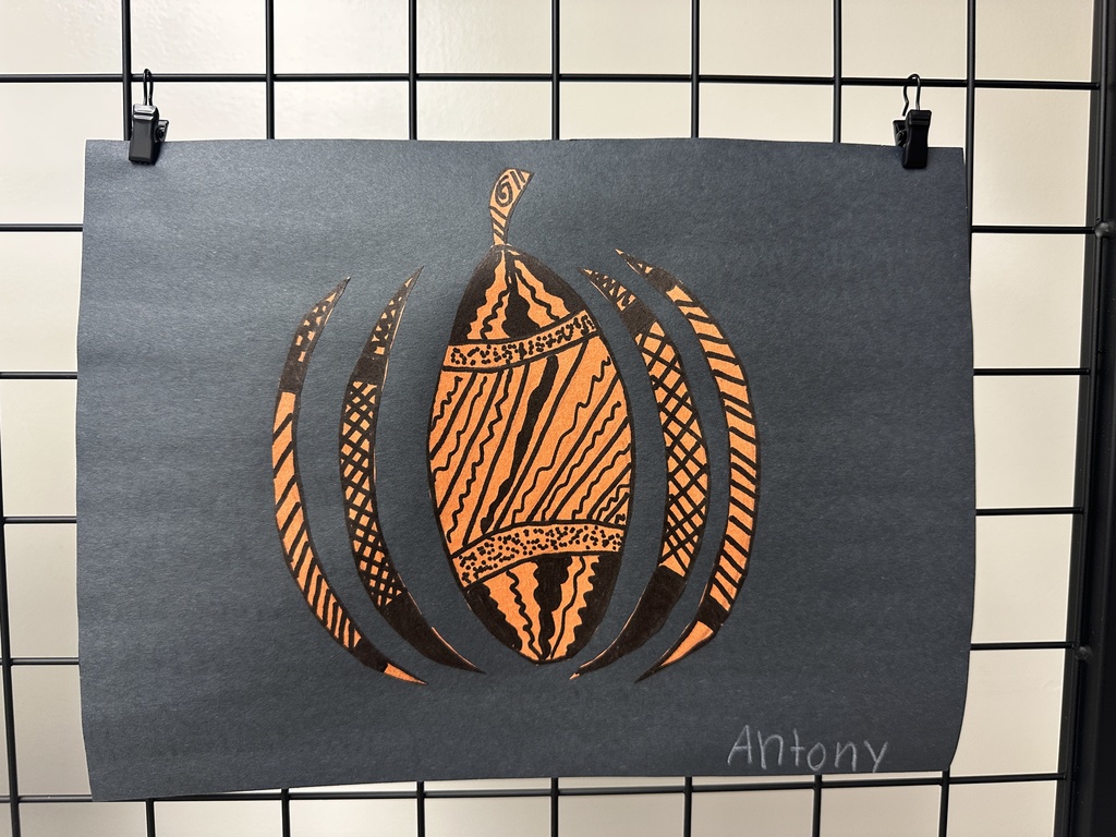 A cut-paper pumpkin shape with bold black patterns and orange backing displayed on dark paper.