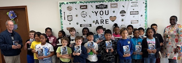students holding dictionaries in front of a bulletin board with different uplifting phrases