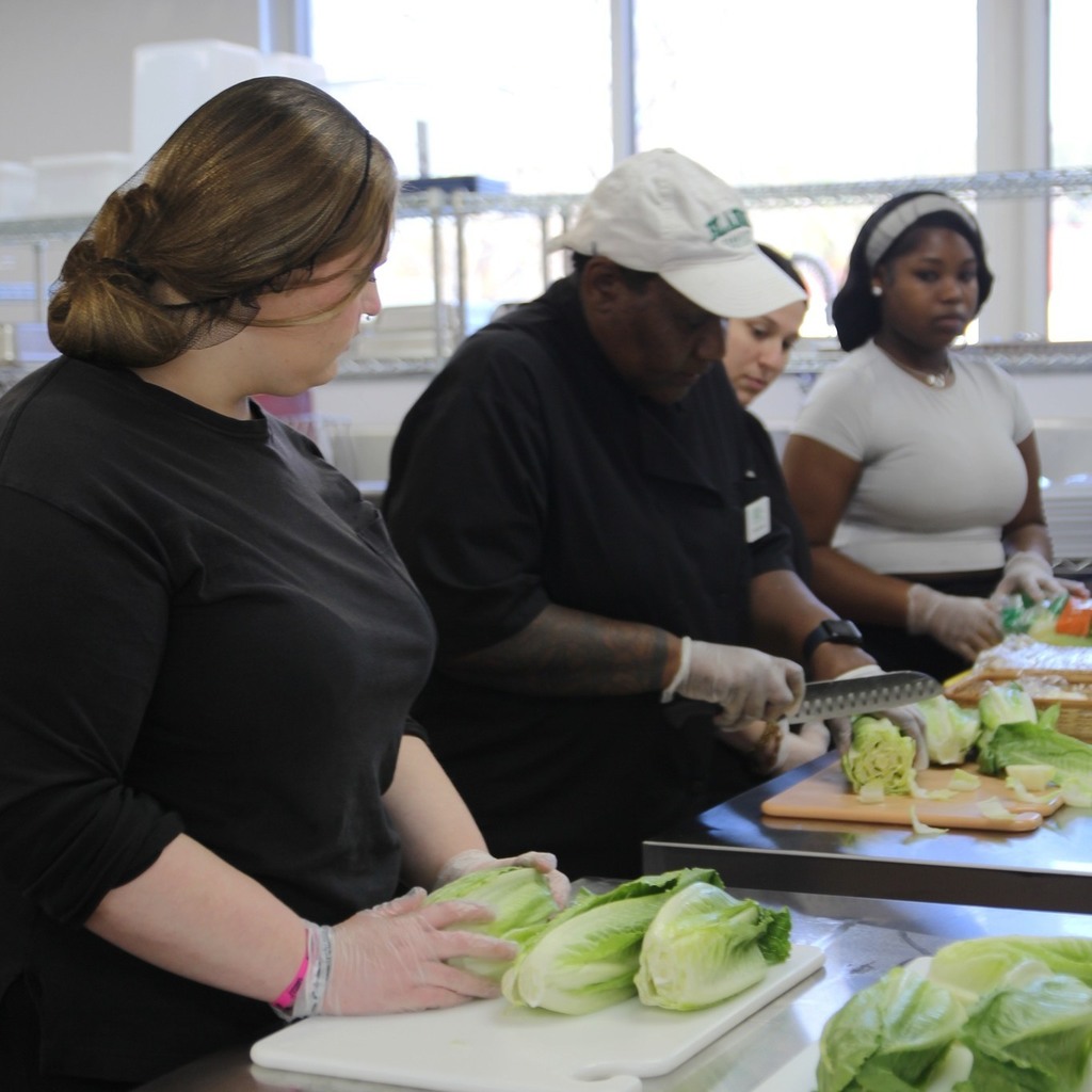 Students and an instructor prepare lettuce together at a kitchen workstation.