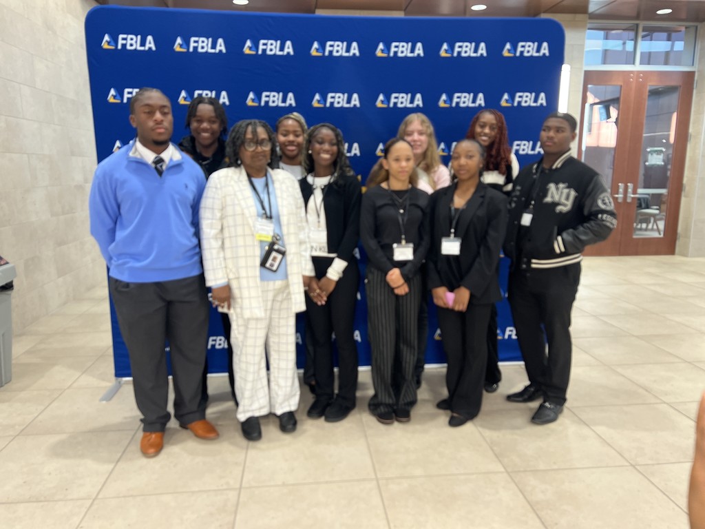 Nine FBLA students and an advisor pose for a group photo in front of a blue backdrop at a conference.