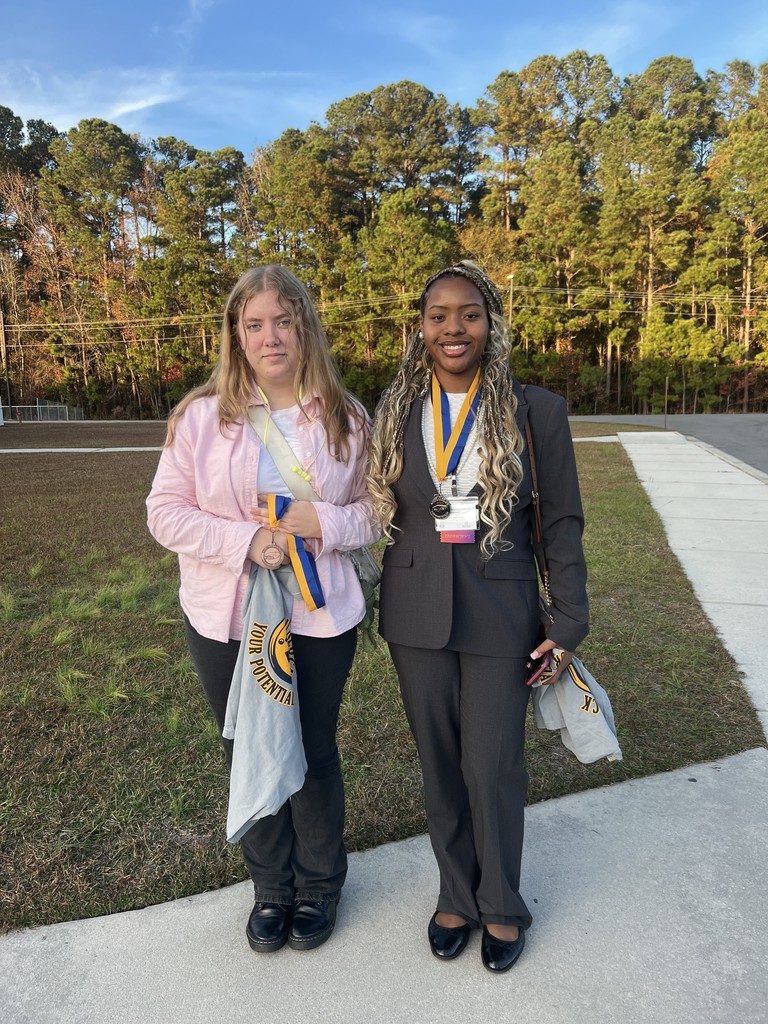 Two female FBLA students stand outside, wearing professional attire and competition award ribbons.