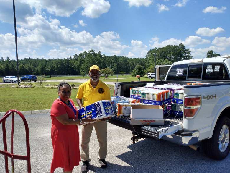 A woman and a man hold a box of paper towels together beside a pickup truck loaded with donated school supplies.
