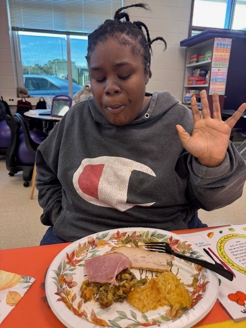 a student waves while seated for a thanksgiving meal