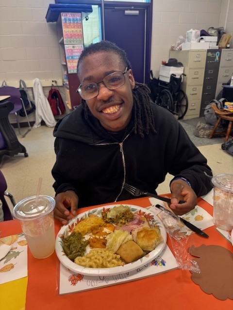 a smiling student eat a plate of food in a classroom
