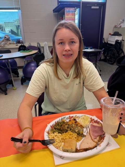 a smiling student eats a plate of food and hold a cup of water