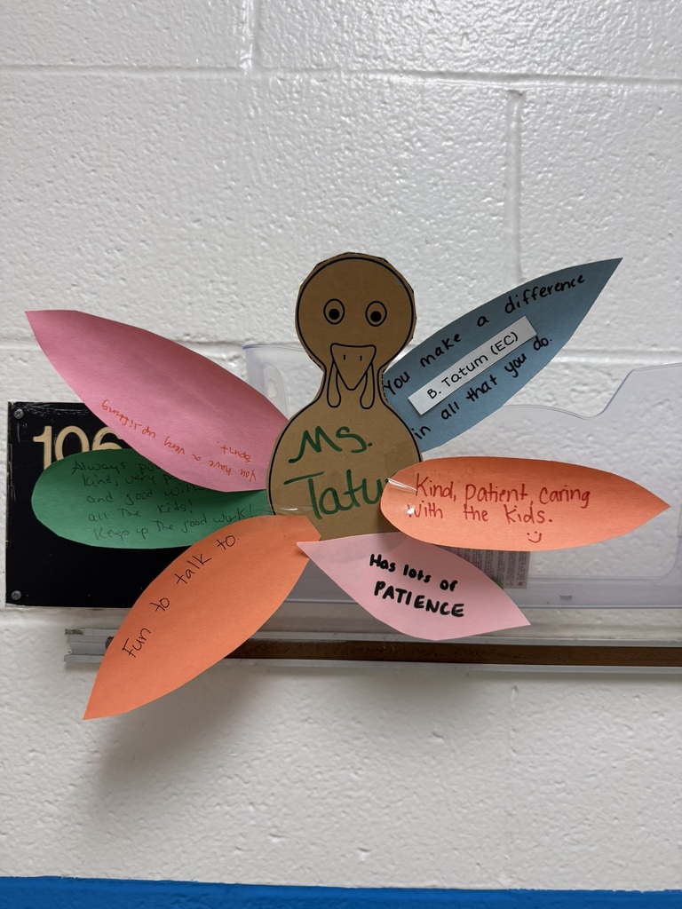Colorful turkey craft with a paper body and vibrant feather-shaped notes expressing gratitude and appreciation, created by students on a wall.