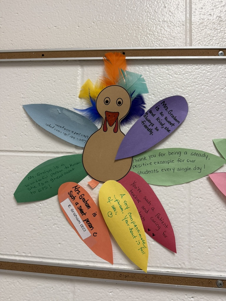 Colorful turkey craft with a paper body and vibrant feather-shaped notes expressing gratitude and appreciation, created by students on a wall.
