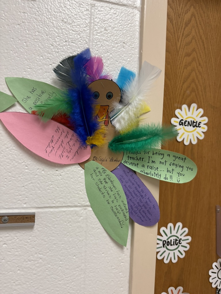 Colorful turkey craft with a paper body and vibrant feather-shaped notes expressing gratitude and appreciation, created by students on a wall.