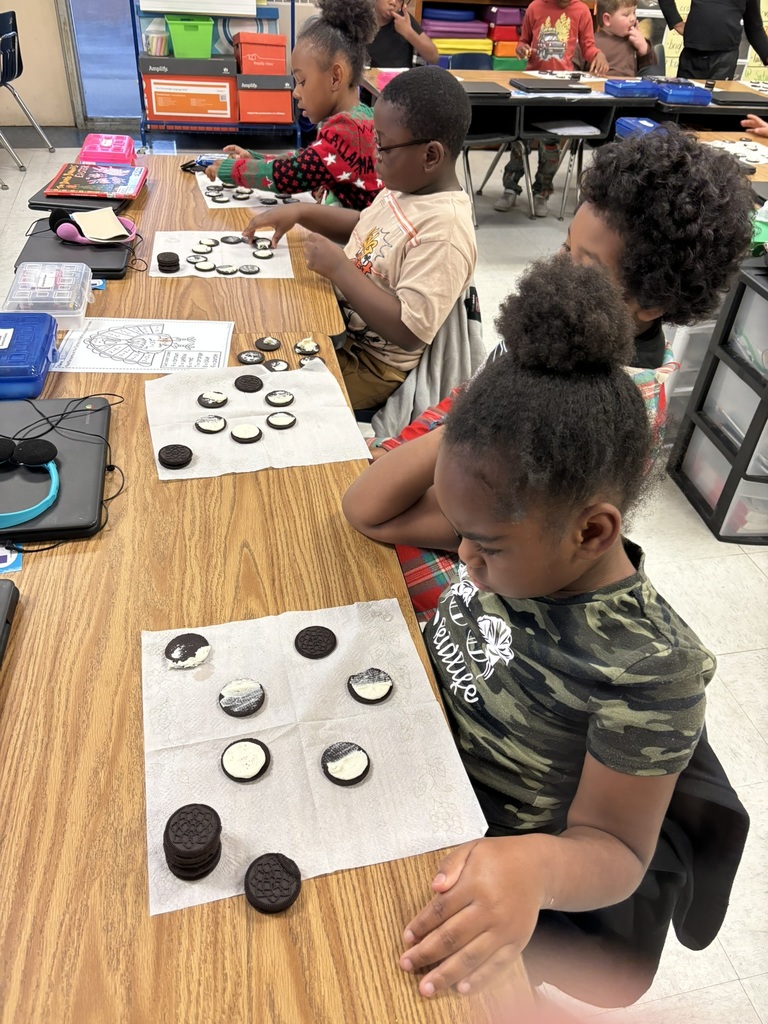 Several students sit at a long table in a classroom, arranging Oreo cookies to show moon phases. Each student has a napkin layout with cookies displaying different amounts of cream to represent waxing and waning phases.