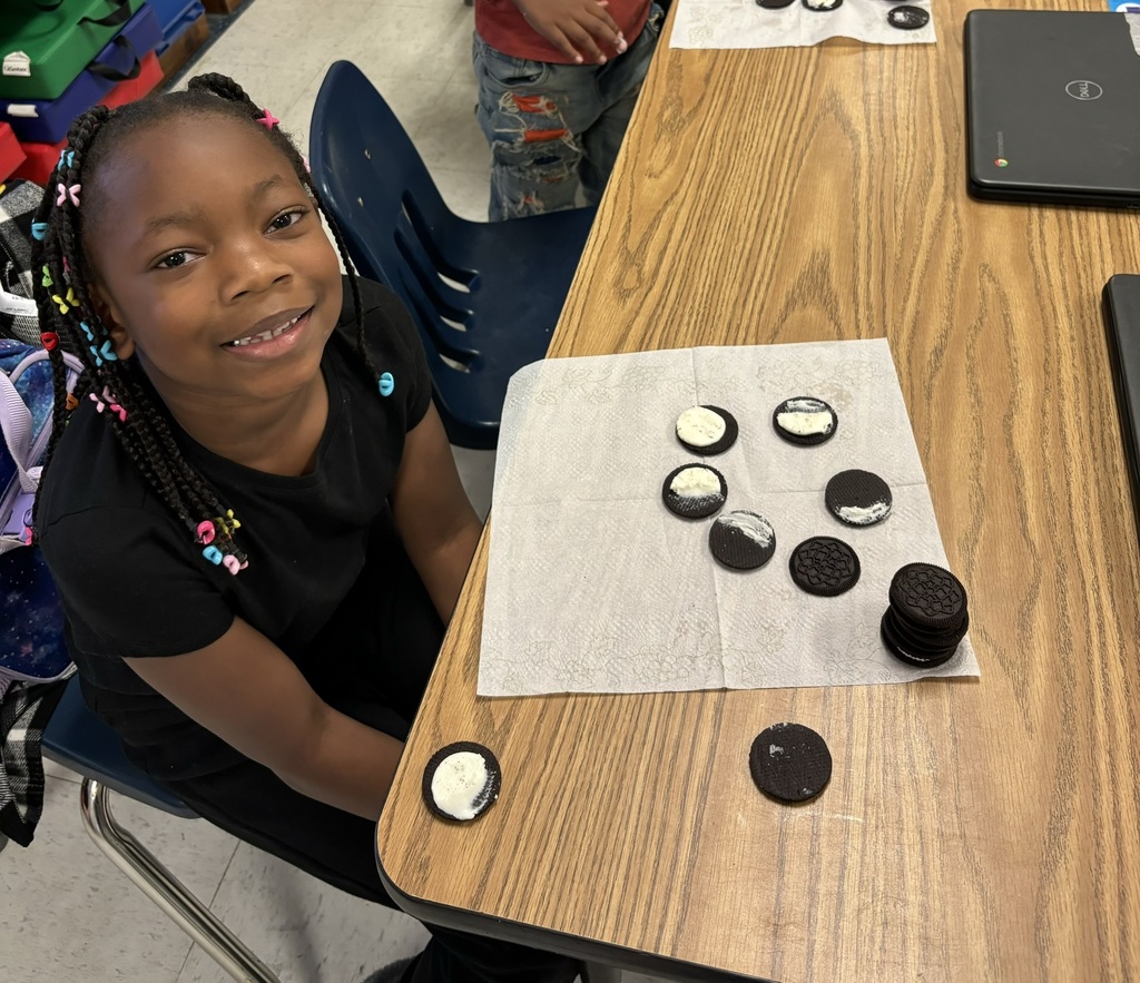 A smiling student sitting at a table with Oreo cookies arranged to display the moon phases on a napkin in front of her.