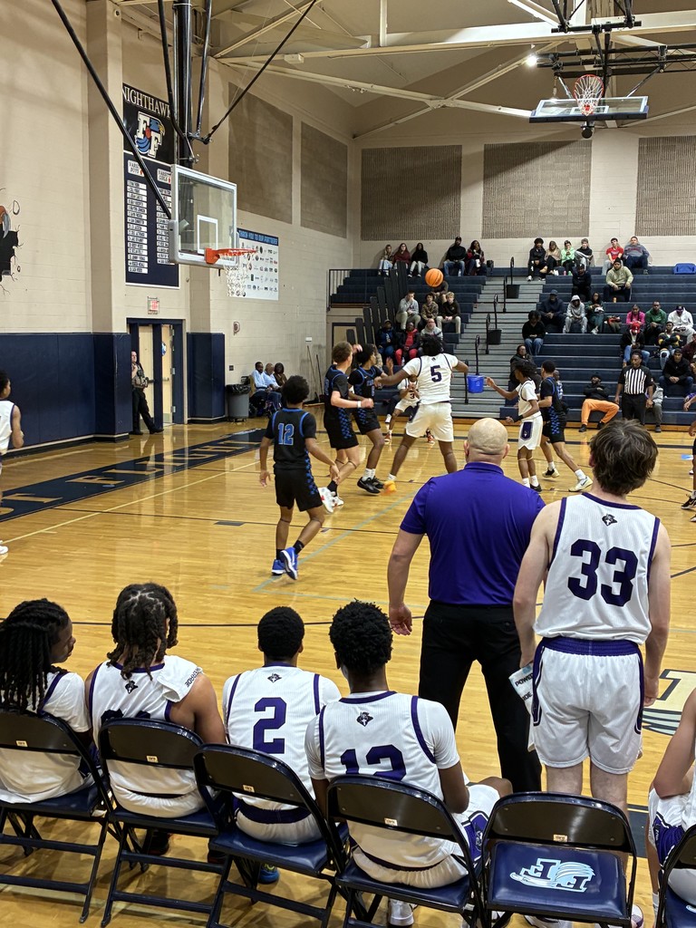 Several basketball players in purple and black uniforms practice dribbling and shooting on a gym court.