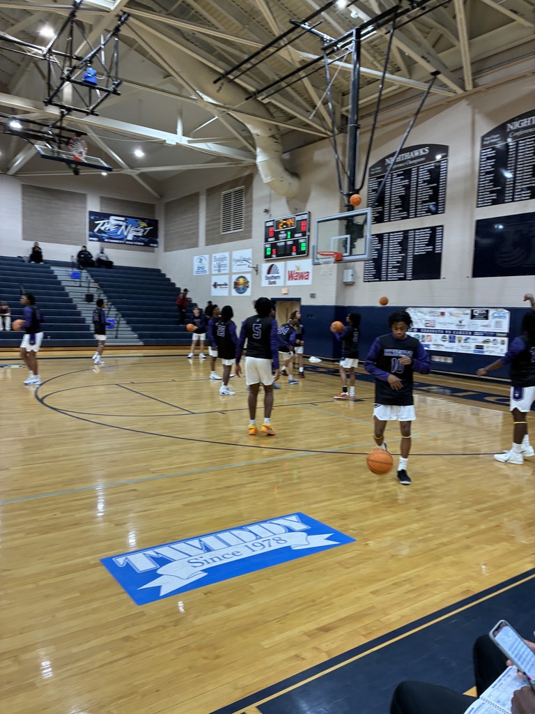 Several basketball players in purple and black uniforms practice dribbling and shooting on a gym court.