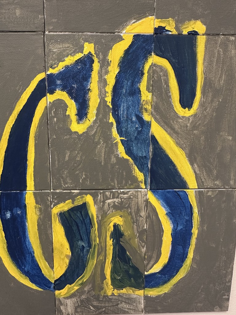 Painted blue and yellow curved letter on gray tiles, forming part of a larger school mural created from small canvases.