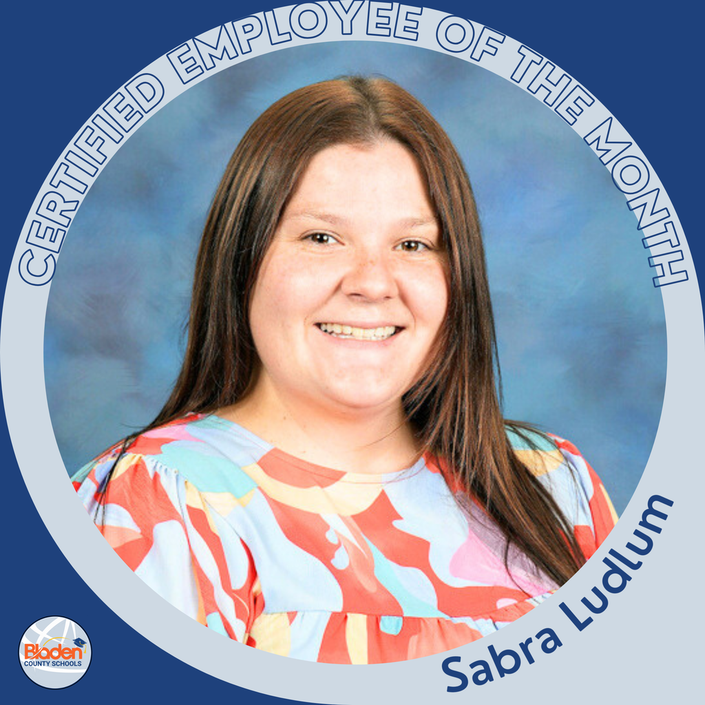 A woman with long brown hair smiles at the camera against a blue studio-style background. She is wearing a colorful patterned blouse. A circular blue-and-gray graphic frame reads “Certified Employee of the Month,” with “Sabra Ludlum” at the bottom and the Bladen County Schools logo in the corner.