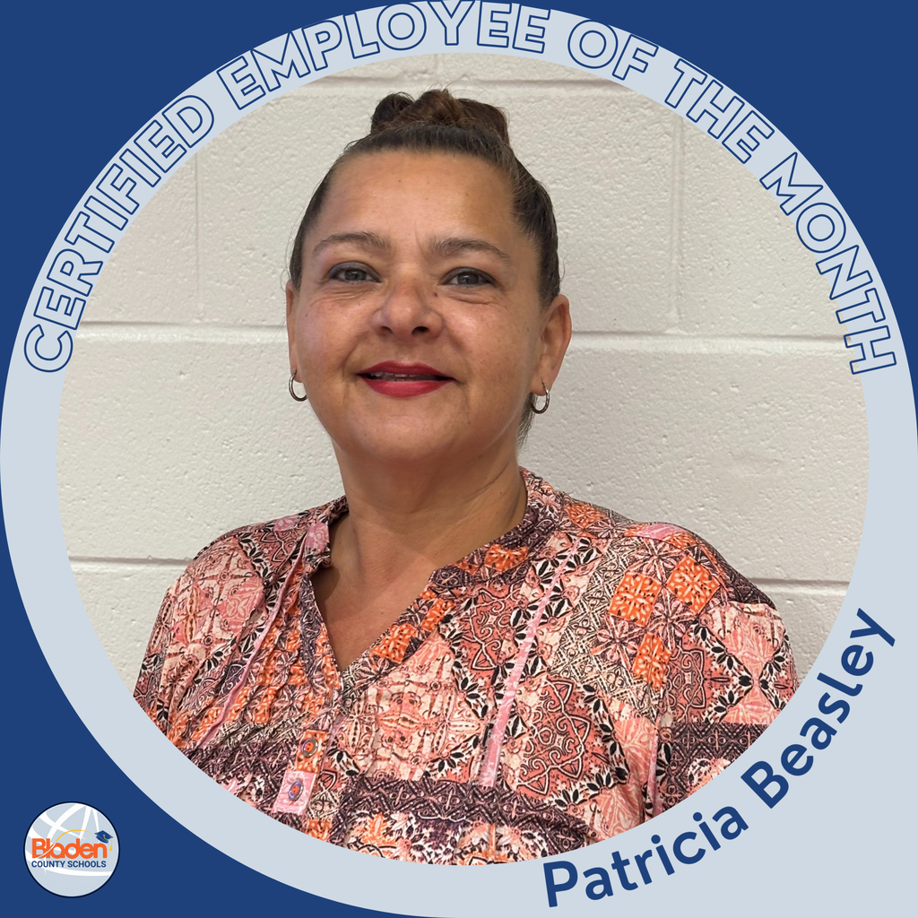 A woman wearing a patterned pink and orange blouse smiles while standing against a light-colored brick wall. She has her hair pulled back and is wearing hoop earrings. The circular frame reads ‘Certified Employee of the Month – Patricia Beasley,’ with the Bladen County Schools logo in the corner.