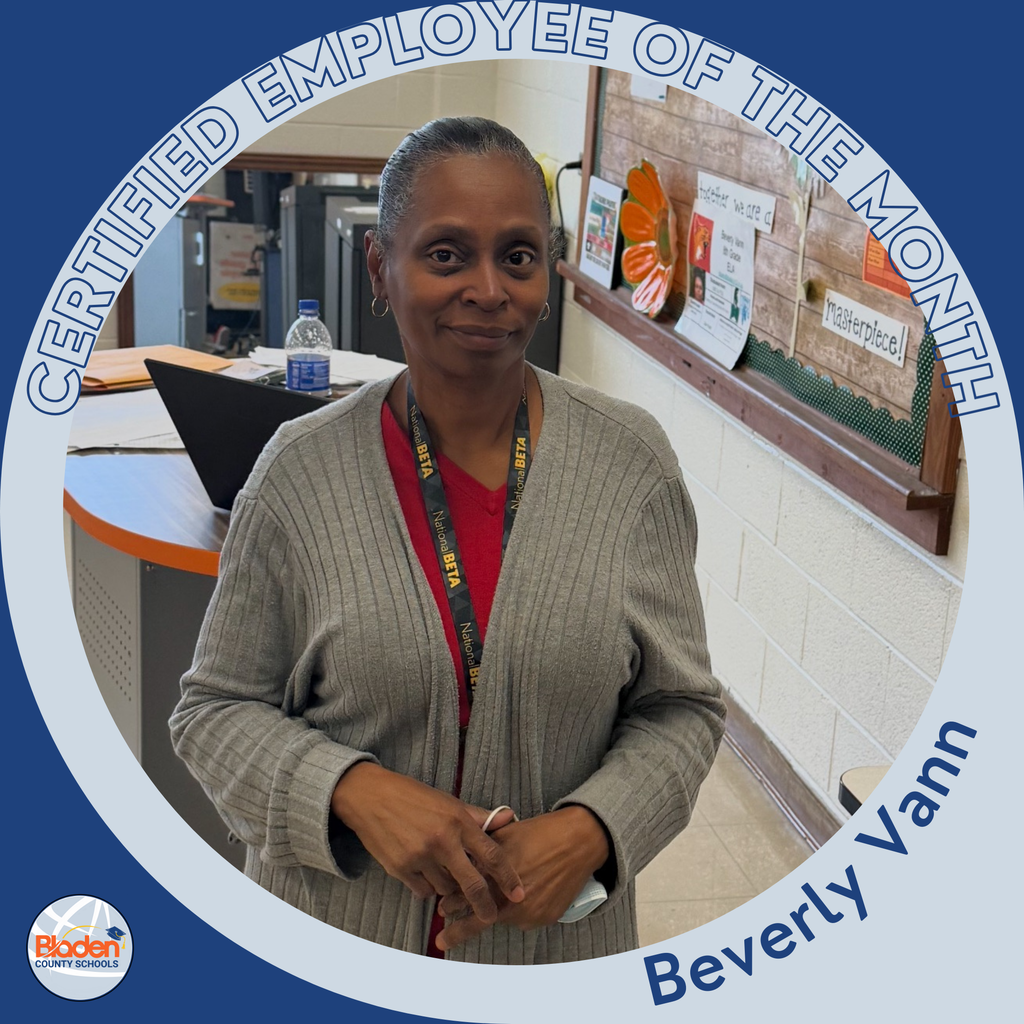 Circular graphic featuring a woman standing in a school office area, wearing a gray cardigan over a red shirt and a lanyard around her neck. The border reads “Certified Employee of the Month,” and the name “Beverly Vann” is displayed along the bottom. A Bladen County Schools logo appears in the lower-left corner.