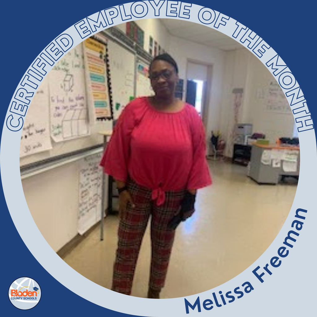 Circular ‘Certified Employee of the Month’ graphic featuring a woman standing in a classroom with whiteboards, posters, and student desks visible. She is wearing a bright pink blouse and plaid pants. Text on the graphic reads ‘Melissa Freeman.