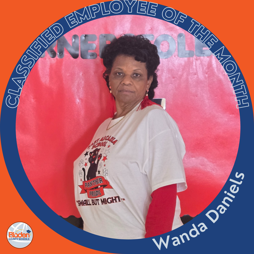 A woman stands in front of a red background wearing a white T-shirt with a panther graphic and the words “Panther Pride: Small But Mighty.” She also wears red earrings and a red sleeve underneath the shirt. A circular orange-and-blue frame reads “Classified Employee of the Month,” with “Wanda Daniels” at the bottom and the Bladen County Schools logo in the corner.