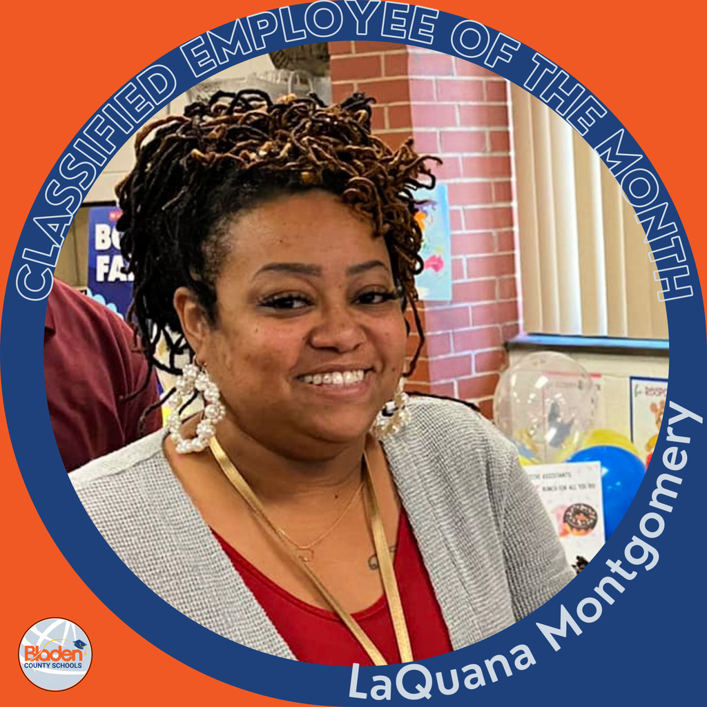 A woman smiling while wearing a red shirt and gray cardigan stands in front of a classroom display with balloons and posters. The circular frame reads ‘Classified Employee of the Month – LaQuana Montgomery.