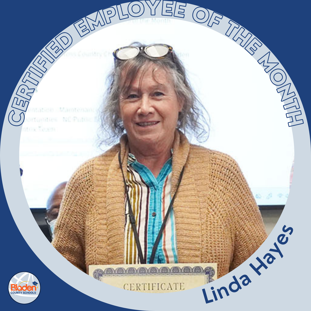 A woman with gray hair wearing glasses on her head, a striped shirt, and a tan knitted cardigan smiles while holding a certificate. The circular frame reads ‘Certified Employee of the Month – Linda Hayes,’ with the Bladen County Schools logo in the corner.