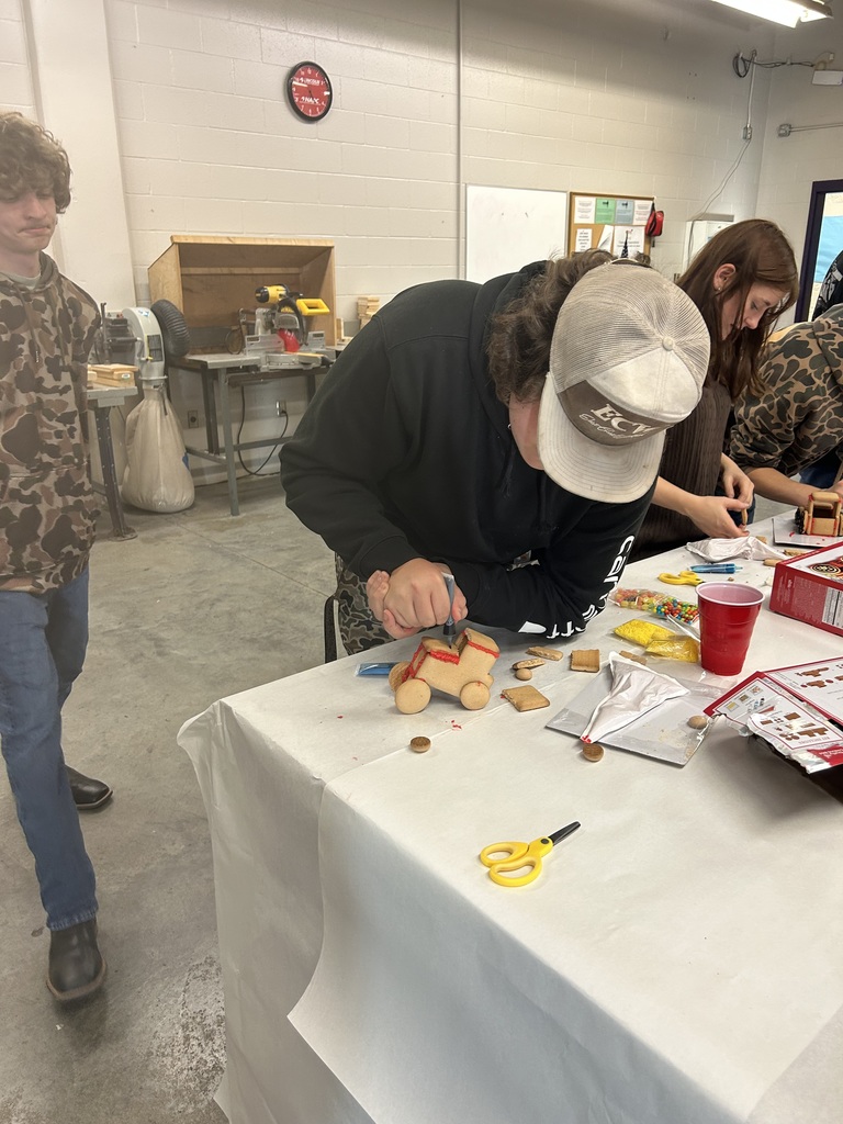 a student carefully adds red icing to a gingerbread tractor
